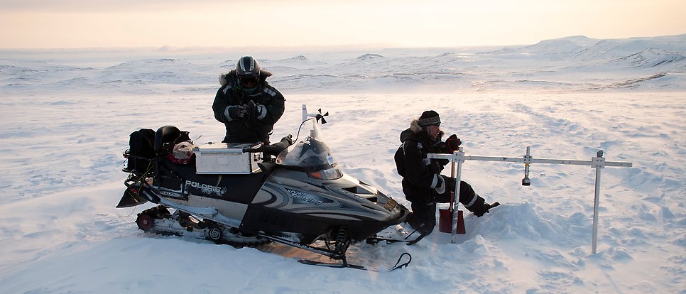 Två personer med snöskoter arbetar på isfält.