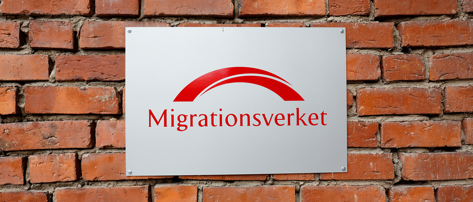 Migrationsverketskylt mot röd tegelvägg.